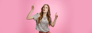 Girl dancing celebrating birthday party having fun carefree folding lips satisfied moving music rhythm pointing fingers up joyfully standing happy pleased pink background, wearing glamour blouse